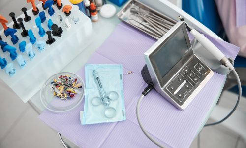 Dental drill with controller unit, burs, cartridge syringe, tray with tweezers and rack with composite resins standing on table